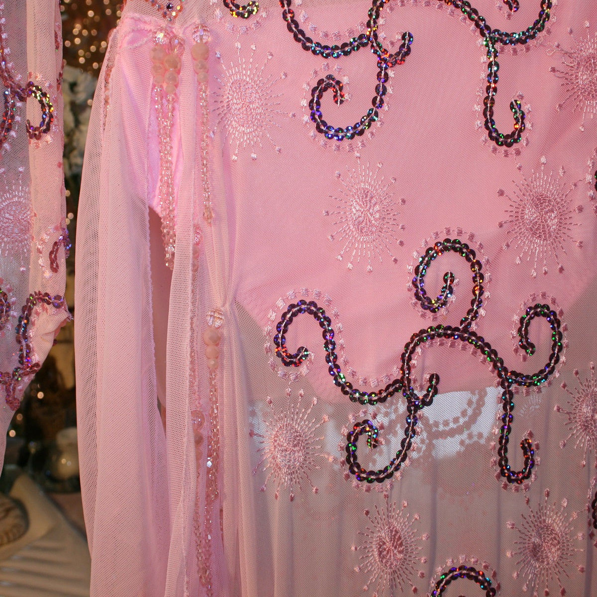 side bead details of  stunning pink Latin-Rhythm dress. Its delicate soft pink stretch mesh is adorned with a mesmerizing scroll design, highlighted by two shades of glimmering pink rhinestones in a beautiful scroll design on the back, upper bodice, and left sheer side. The extensive hand beading in the skirting adds the perfect touch of elegance